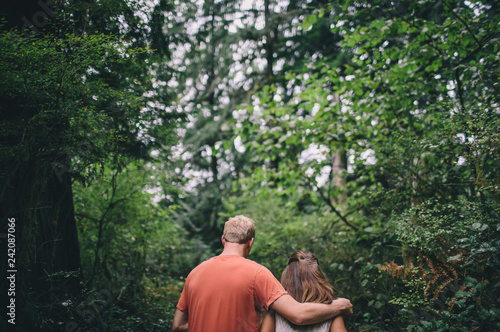 couple walking on pathway in forest man hands over shoulder