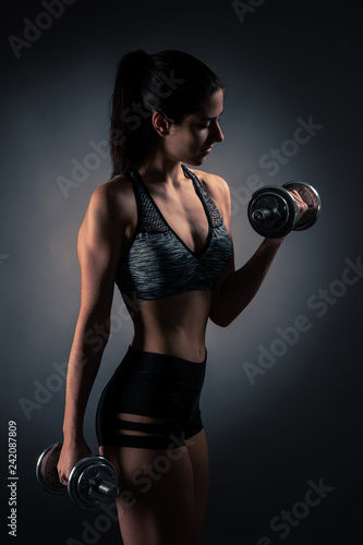 Beautiful young woman workout with dumbbell over gray background in fitness gym club