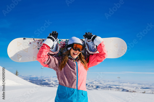 happy cheerful woman in a ski suit and glasses holds a snowboard in her hands in winter. Extreme