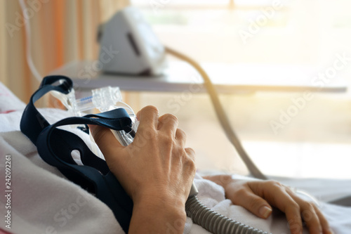 Obstructive sleep apnea therapy..Close up of senior patient woman hand holding Cpap mask between the chest lying  in hospital room.