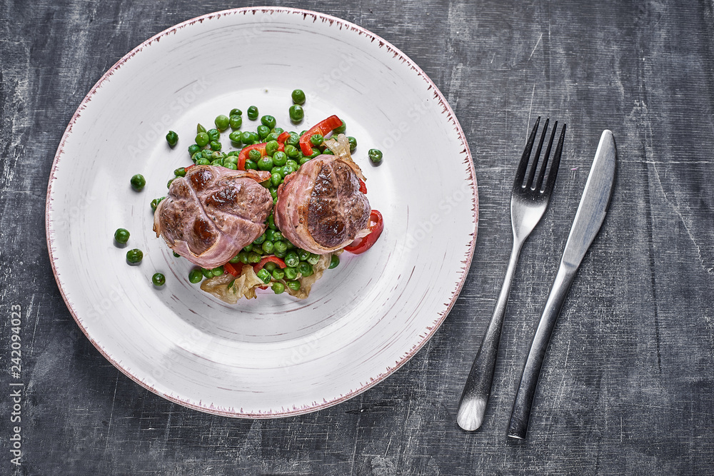 Beef medallions wrapped in bacon, serve with green peas and on a plate on wooden background. Close up Beef medallions wrapped in bacon, serve with green peas and on a plate on wooden background. Close up