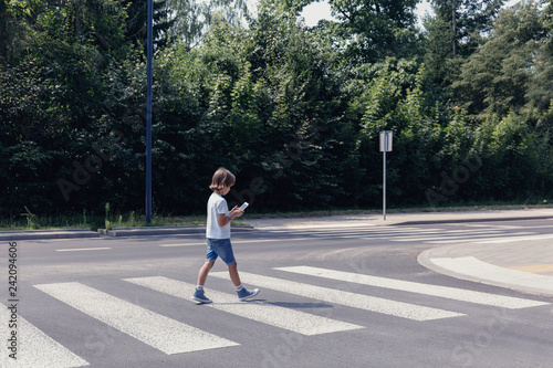 Fotografie Boy crossing the street while looking at his smartphone