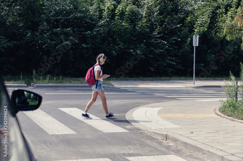 Young girl crossing a street while listening to music and looking at smartphone