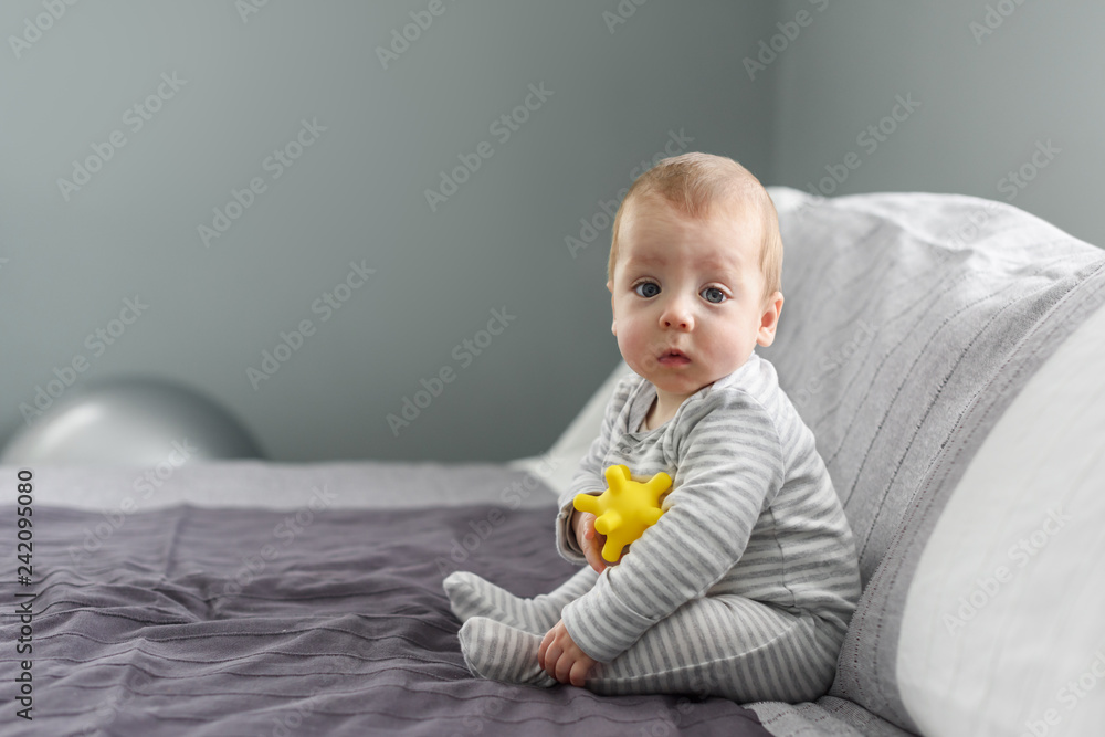Sitting baby boy on grey carpet with yellow ball toy. Motherhood and new life concept Sitting baby boy on grey carpet with yellow ball toy. Motherhood and new life concept