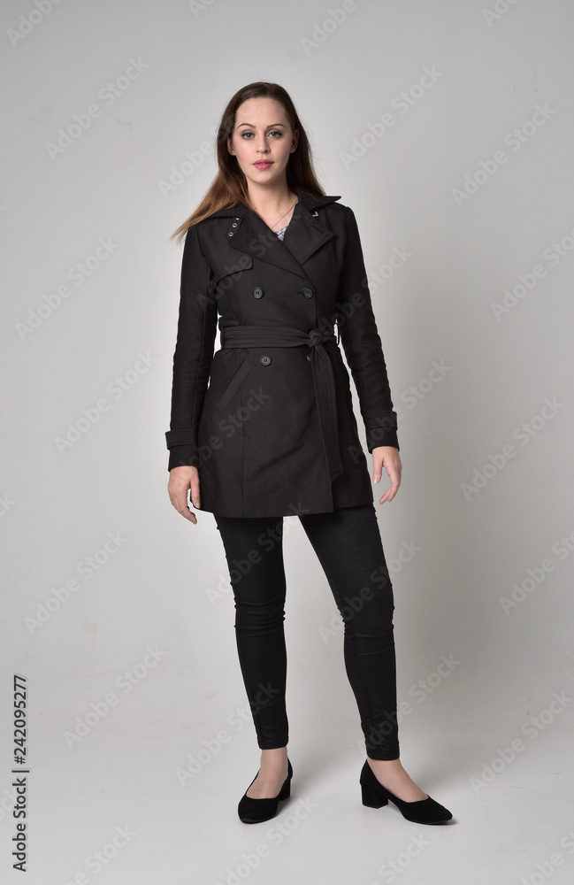 full length portrait of a brunette girl wearing long black coat, standing pose on grey studio background. full length portrait of a brunette girl wearing long black coat, standing pose on grey studio background.