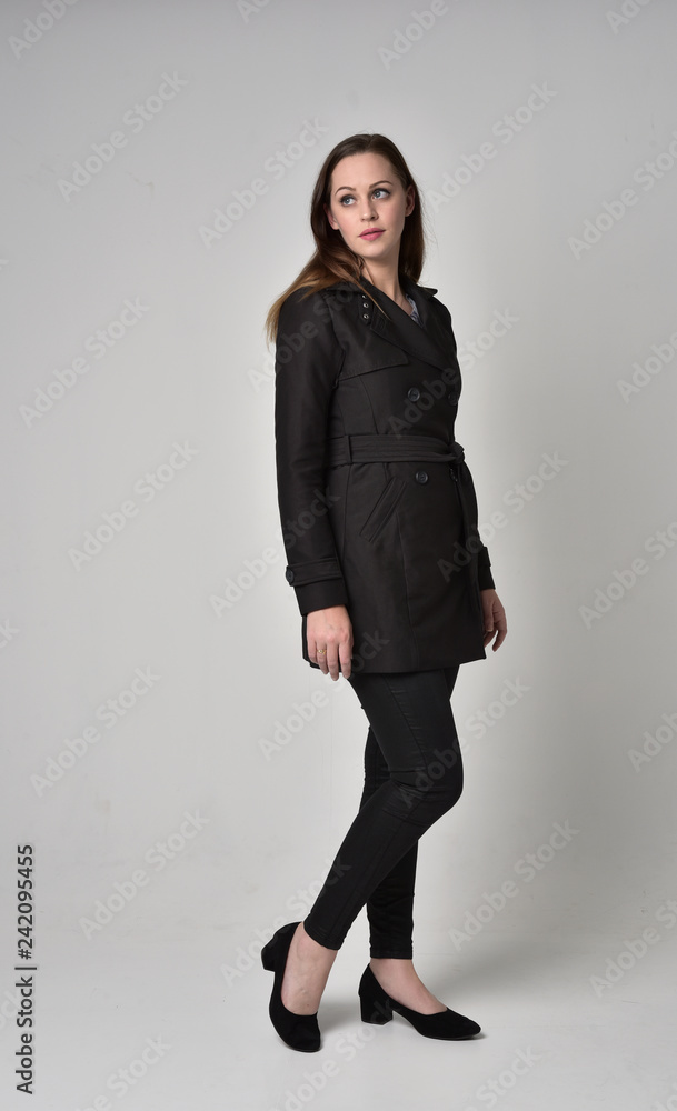 full length portrait of a brunette girl wearing long black coat, standing pose on grey studio background. full length portrait of a brunette girl wearing long black coat, standing pose on grey studio background.