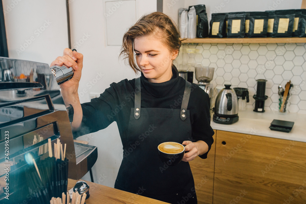 Young owner female barista in black uniform holding cup of cappuccino working coffee machine in modern coffee shop. Coffee business entrepreneur owner concept. foto de Stock | Adobe Stock