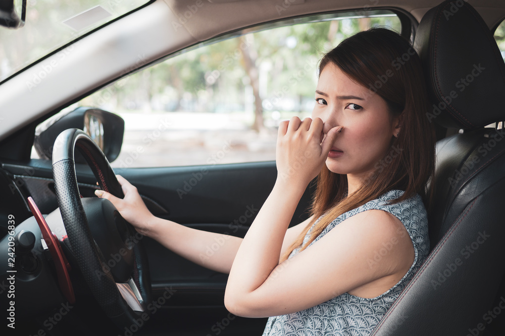 Young woman holding her nose because of bad smell in car