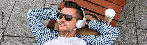 Young man with headphones lying on a park bench outdoors photo