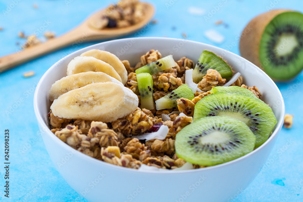 Dry breakfast cereals. Crunchy honey muesli bowl with slices of fresh banana and kiwi on a blue background. Raw diet and fiber food. Breakfast time Dry breakfast cereals. Crunchy honey muesli bowl with slices of fresh banana and kiwi on a blue background. Raw diet and fiber food. Breakfast time
