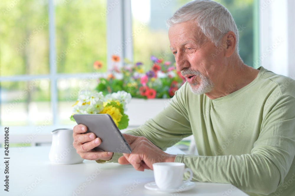 senior man using tablet while drinking tea senior man using tablet while drinking tea