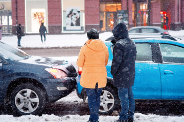 Drivers look at damaged cars after road accident in blizzard. Car crash accident on winter road with snow, unsafe distance when driving on slippery roads. Winter driving - car breakdown