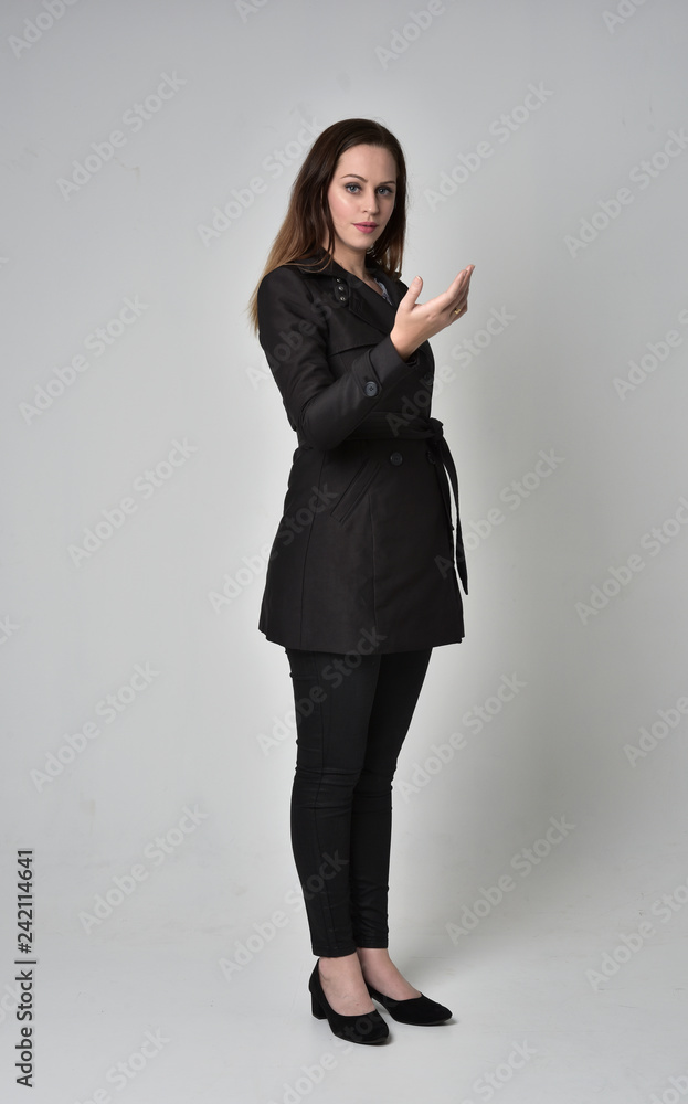 full length portrait of a brunette girl wearing long black coat, standing pose on grey studio background. full length portrait of a brunette girl wearing long black coat, standing pose on grey studio background.