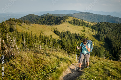Plus size young pretty brunette woman backpacking in summer at the mountains. Outdoor activity concept. Health life and summer vacation concept. Sunny summer evening at Ukrainian Carpathians.