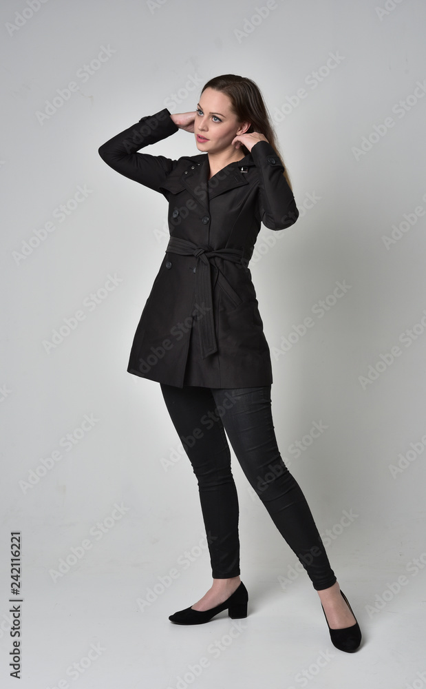 full length portrait of a brunette girl wearing long black coat, standing pose on grey studio background. full length portrait of a brunette girl wearing long black coat, standing pose on grey studio background.