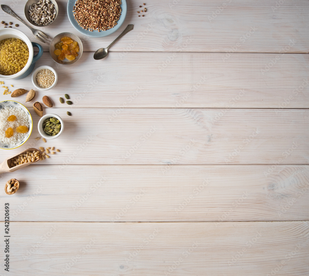 Different nuts, cereals, raisins on plates on a wooden table. Cedar, cashew, hazelnut, walnuts, almonds, pumpkin seeds, sunflower seeds, bulgur, buckwheat, rice and a spoon on the table. Different nuts, cereals, raisins on plates on a wooden table. Cedar, cashew, hazelnut, walnuts, almonds, pumpkin seeds, sunflower seeds, bulgur, buckwheat, rice and a spoon on the table.