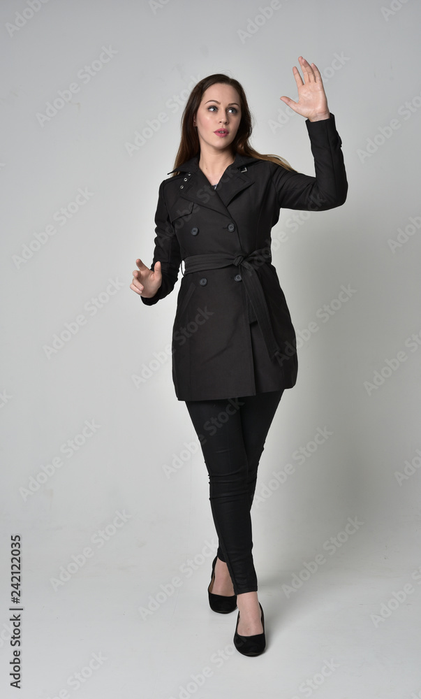 full length portrait of a brunette girl wearing long black coat, standing pose on grey studio background. full length portrait of a brunette girl wearing long black coat, standing pose on grey studio background.