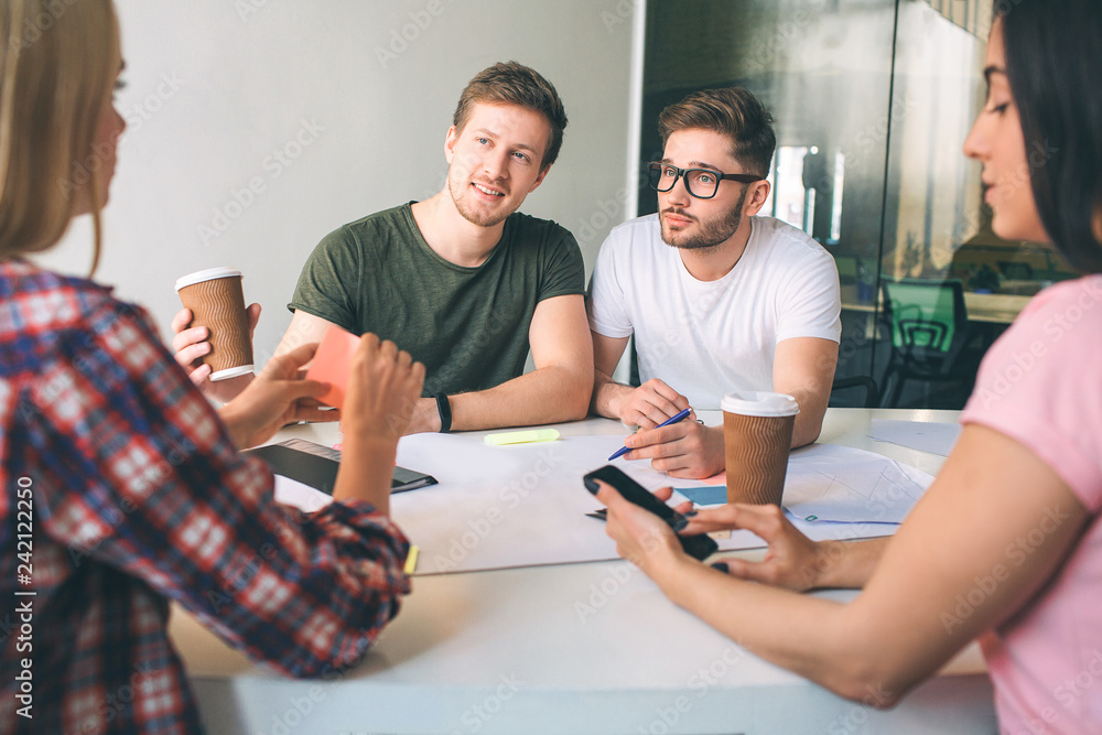 Nice and cheerful young men look at young blonde woman. They smile a bit. Brunette hold phone in hands. THey sit at table in white room. Nice and cheerful young men look at young blonde woman. They smile a bit. Brunette hold phone in hands. THey sit at table in white room.