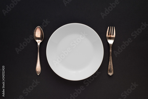White plate, spoon and fork, on a black background