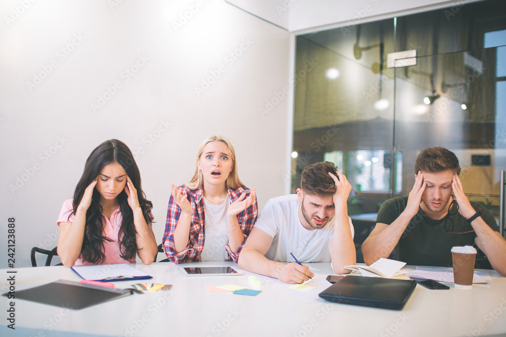 Amazed and upset young blonde woman look on camera. She scream. Other people trying to concentrate. They do brainstorming. All of them sit together in white room. Amazed and upset young blonde woman look on camera. She scream. Other people trying to concentrate. They do brainstorming. All of them sit together in white room.