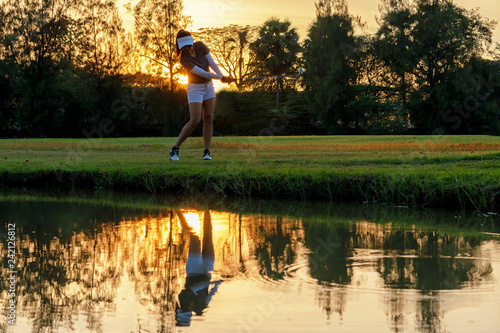 Healthy Sport. Asian Sporty woman golfer player chips and swing golf on the green sunset evening time, she presumably does exercise.  Healthy Lifestyle Concept. © freebird7977