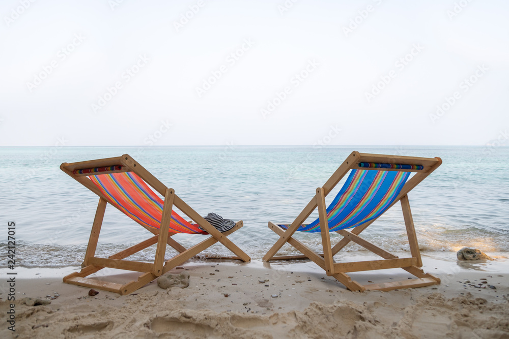 The orange and blue beach chair are on the clear sand beach with sea in background The orange and blue beach chair are on the clear sand beach with sea in background