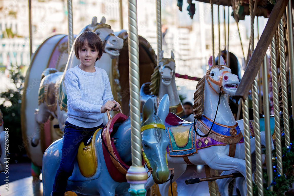 Sweet boys, brothers, riding in a Santa Claus sledge on a merry-go-round, carousel attraction in Europe, active children