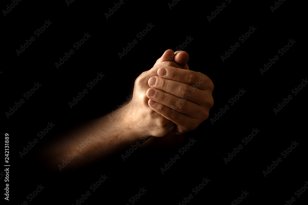 Men's hands in prayer on a black background. The concept of faith, prayer, mourning, forgiveness, confession.