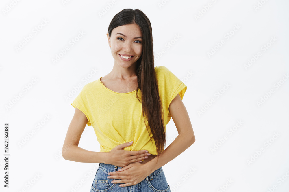 Woman feeling healthy and pleased. Delighted good-looking female with beautiful smile gazing at camera touching stomach with delight and relief curing pain or drinking yogurt and feeling good Woman feeling healthy and pleased. Delighted good-looking female with beautiful smile gazing at camera touching stomach with delight and relief curing pain or drinking yogurt and feeling good