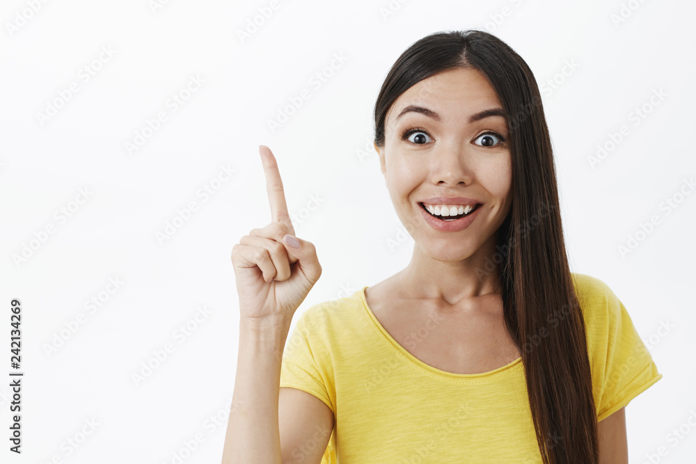 Energized young creative female genius with broad white smile raising index finger in eureka gesture adding suggesting having perfect idea or plan to share with team against gray background Energized young creative female genius with broad white smile raising index finger in eureka gesture adding suggesting having perfect idea or plan to share with team against gray background