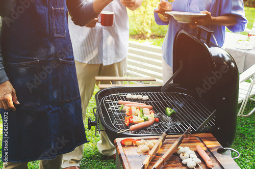 Group of elderly are rotating meat and vegetable on a stick that is being grilled.