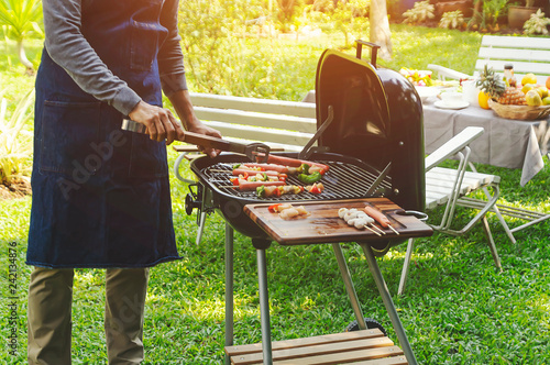 Handsome man preparing barbecue for friends in the garden.- Image