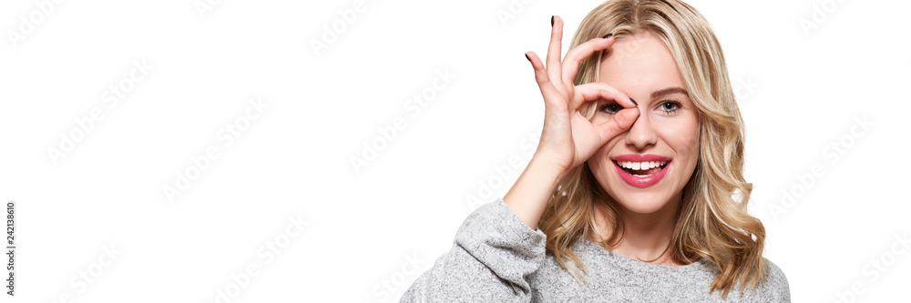 Portrait of beautiful excited woman in casual clothing smiling and showing ok sign at camera isolated over white banner. Portrait of beautiful excited woman in casual clothing smiling and showing ok sign at camera isolated over white banner.