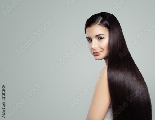 Smiling brunette girl with long healthy hair on gray backgroung, hair care concept