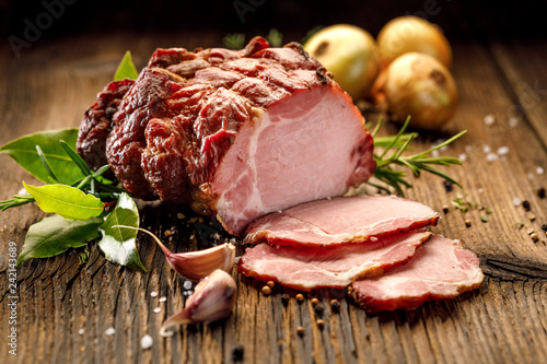 Sliced smoked gammon on a wooden  table with addition of fresh  herbs and aromatic spices Fototapeta