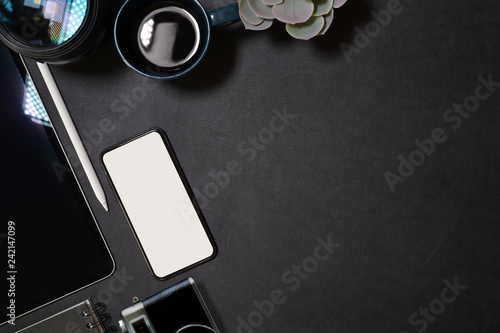 Creative dark leather desk with ฺblank screen mobile phone, tablet, lens and designer gadget
