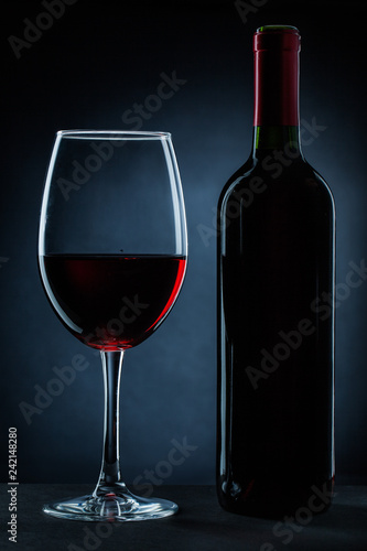 bottle and wineglass with red wine on black.
