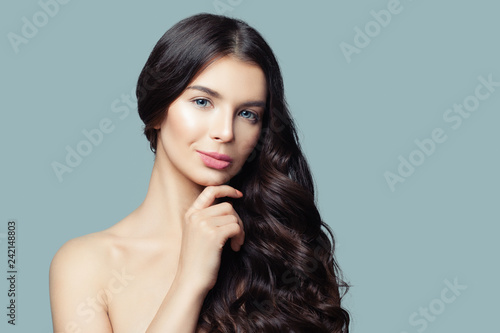 Young healthy woman with long curly hair and natural makeup. Cute female face on blue background