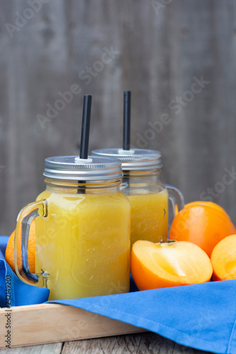 Healthy orange juice with Persimmon, khaki fruits in glass jars, rustic wooden table. Copy space. photo