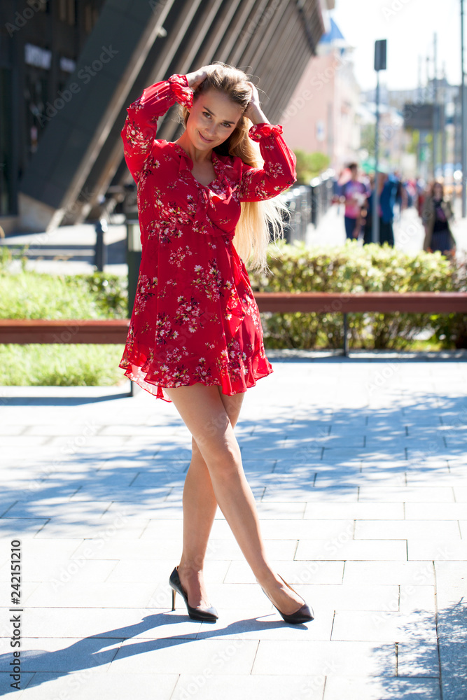 Naklejka premium Sexy blonde model posing on th street in red summer dress