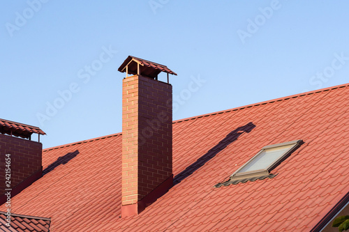 Closeup of skylight and brick chimney on the metal tile roof under blue sky