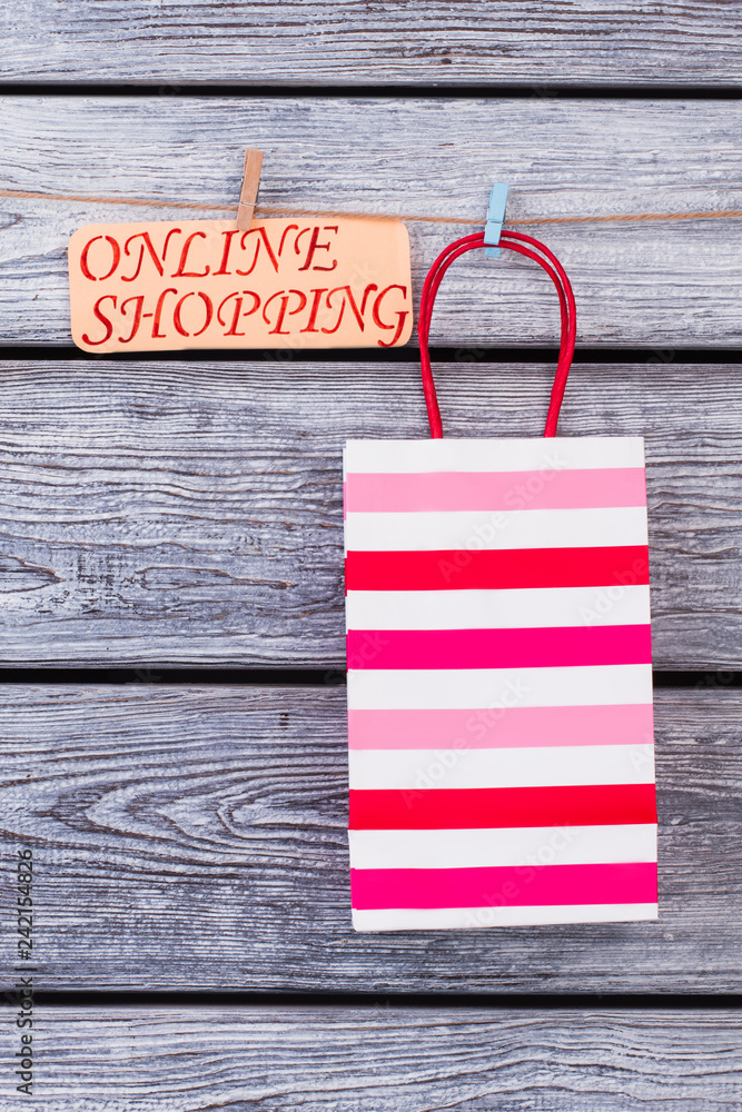 Obraz premium Striped shopping bag on wooden background. Paper gift bag hanging on clothesline with clothespins. Save your time and money.