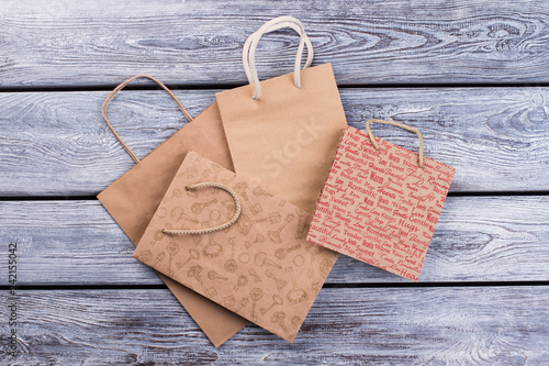Kraft paper shopping bags on wooden background. Four brown carrier paper bags with handles, top view.