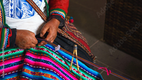 Hands of peruvian woman making alpaca wool carpet with national pattern close-up. Manufacture of wool material in Peru, Cusco. Woman dressed in colorful traditional native Peruvian closing