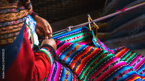 Hands of peruvian woman making alpaca wool carpet with national pattern close-up. Manufacture of wool material in Peru, Cusco. Woman dressed in colorful traditional native Peruvian closing