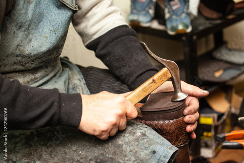 close-up of hands male shoemaker repairing shoes by nailing a heel photo