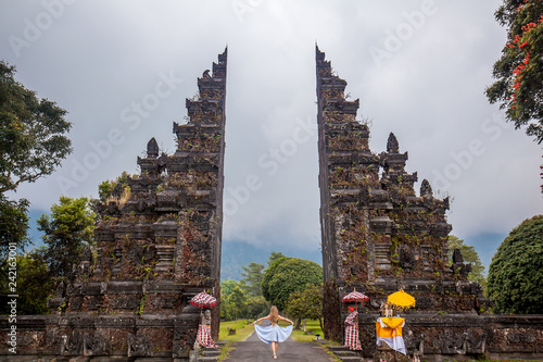 Young woman with long hair dressed in skirt standing at traditional Hindu temples gate (Gapura Handara Kosaido) on the north of Bali island, Indonesia photo