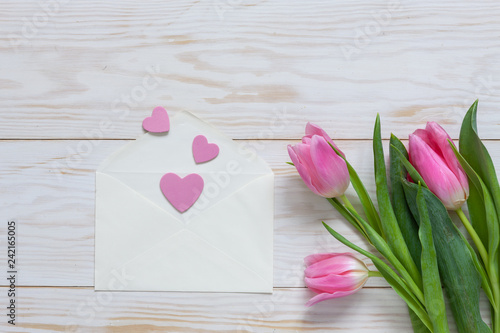 Fototapeta Naklejka Na Ścianę i Meble -  Bouquet  of pink tulips and hearts pattern in paper envelope. Top view, close-up, flat lay on white wooden background
