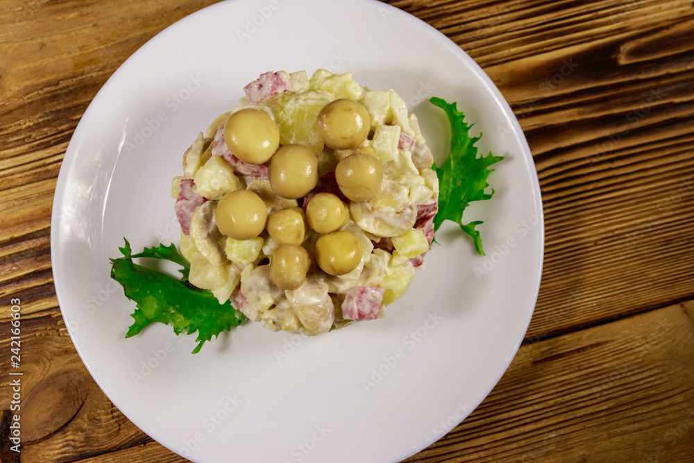 Potato salad with marinated mushrooms, sausage, onion and mayonnaise on wooden table Potato salad with marinated mushrooms, sausage, onion and mayonnaise on wooden table