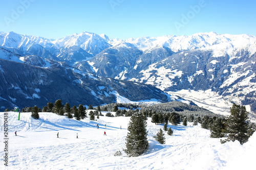 People enjoying skiing on prepared slopes in the Alps on sunny day. Beautiful snowy trees in the mountains. Perfect winter holidays destination for family in modern comfortable Alpine ski resort. 